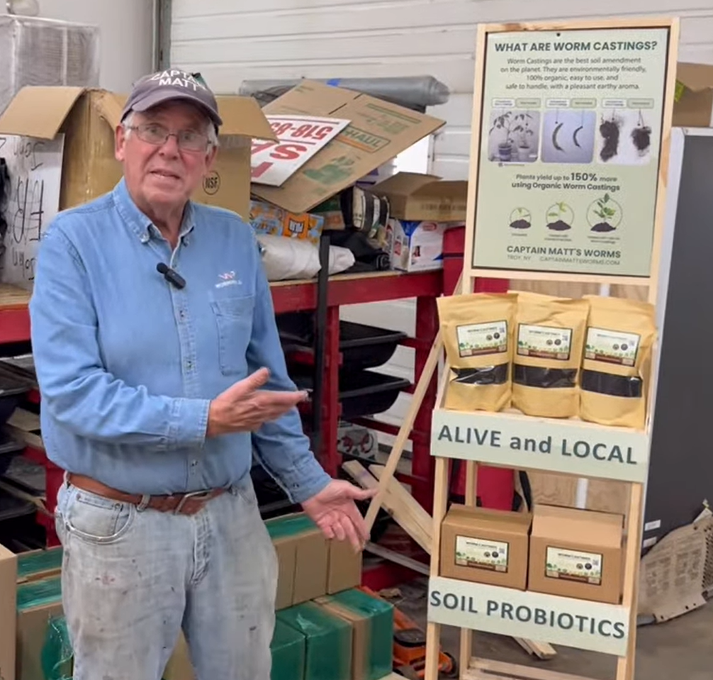 Captain Matt presenting worm castings products and a display explaining their benefits, in a workshop setting
